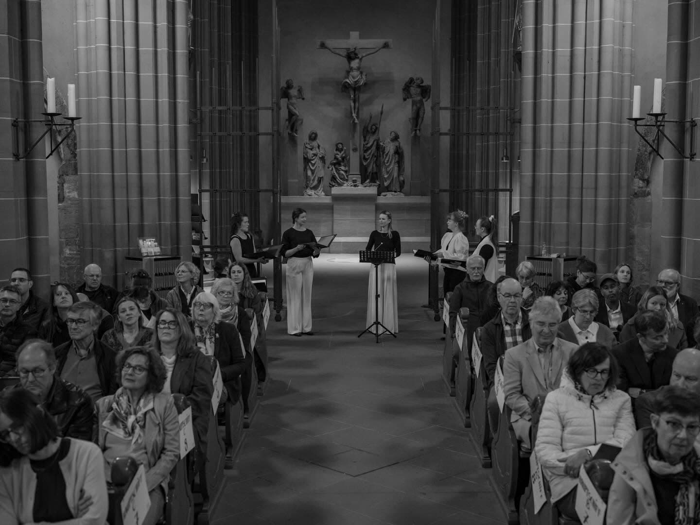 Blick durch den Mittelgang einer vollbesetzten Kirche auf Sjaella, die vor dem Kruzifix singt (Schwarzweiß)